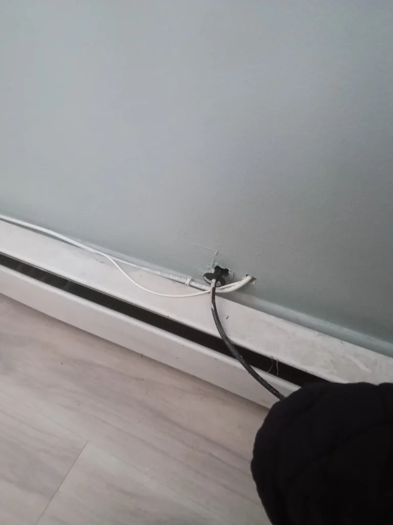 Utility line penetration behind a baseboard, left unsealed and accessible from inside the home.